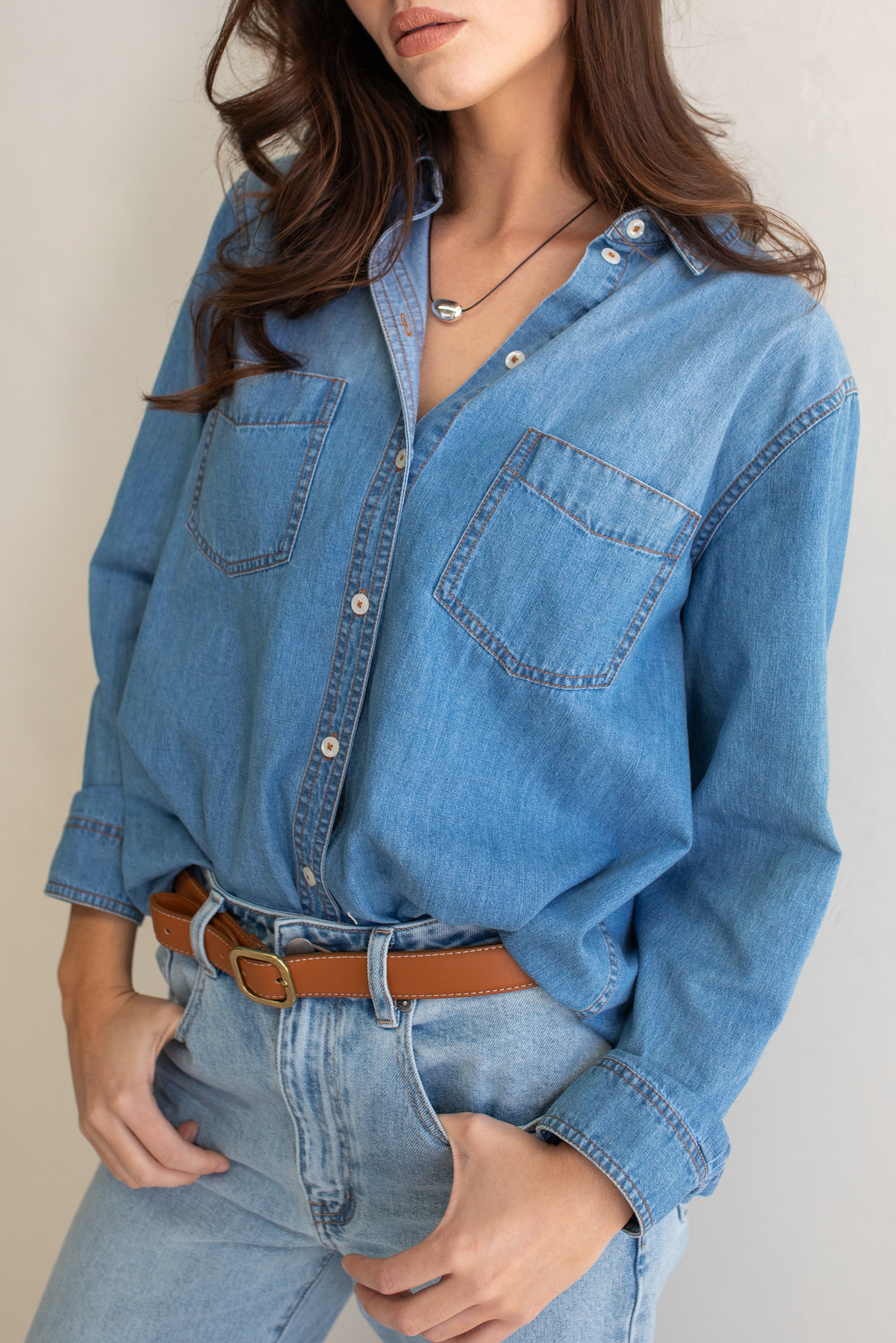 Close up of a Hut blue denim oversized boyfriend shirt and jeans with a neutral background