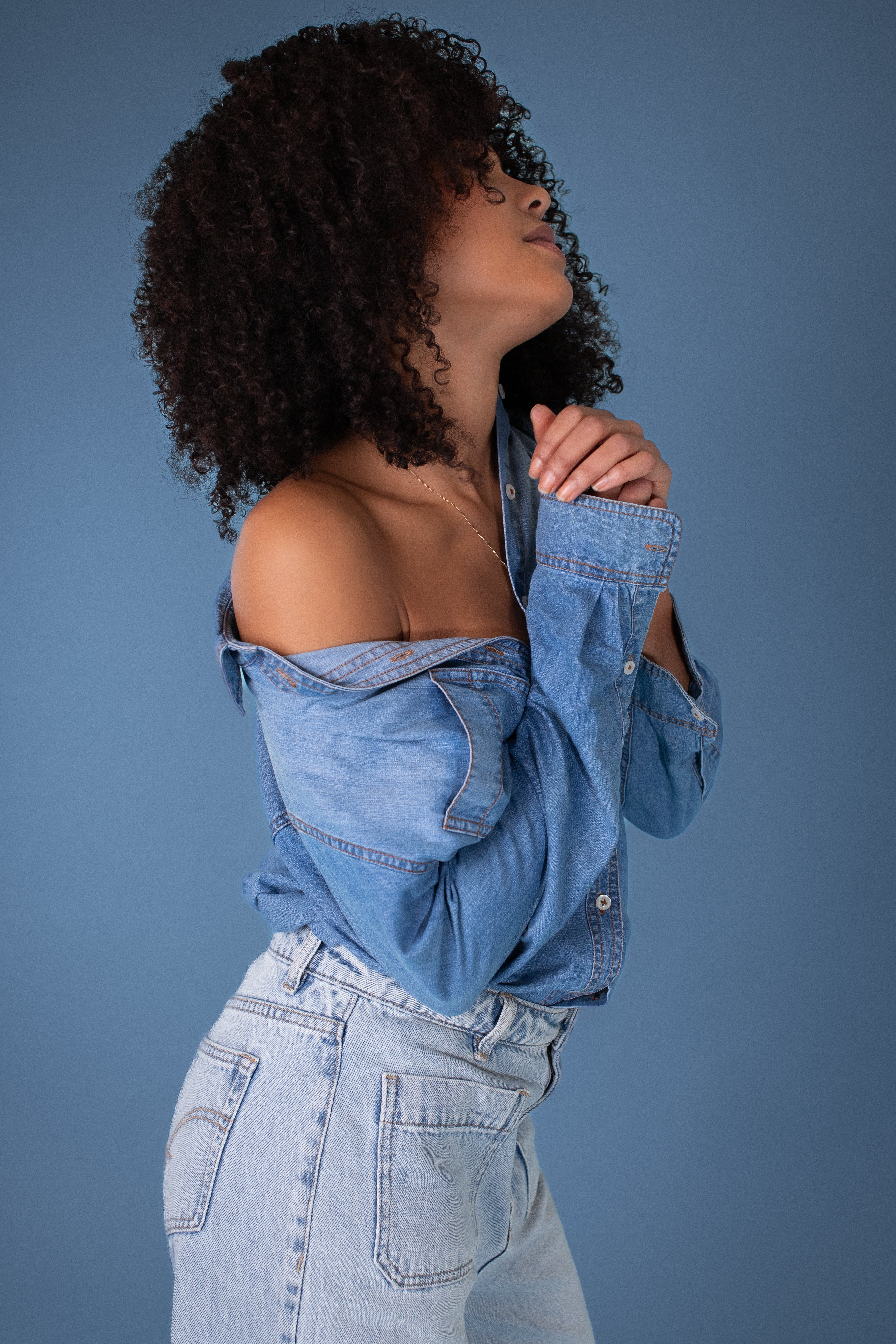 Woman wearing a Hut blue denim shirt and jeans against a blue background
