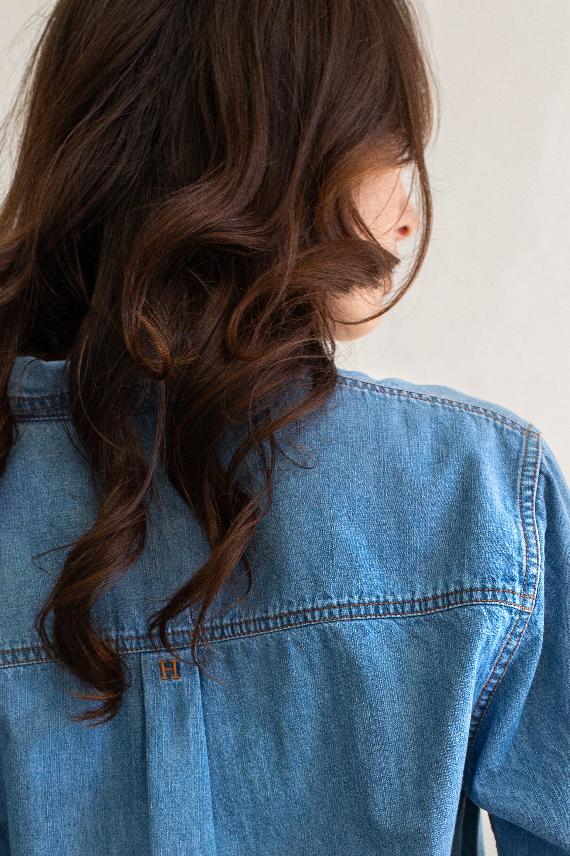 Close up of embroidery on a Hut blue denim oversized shirt with a neutral background
