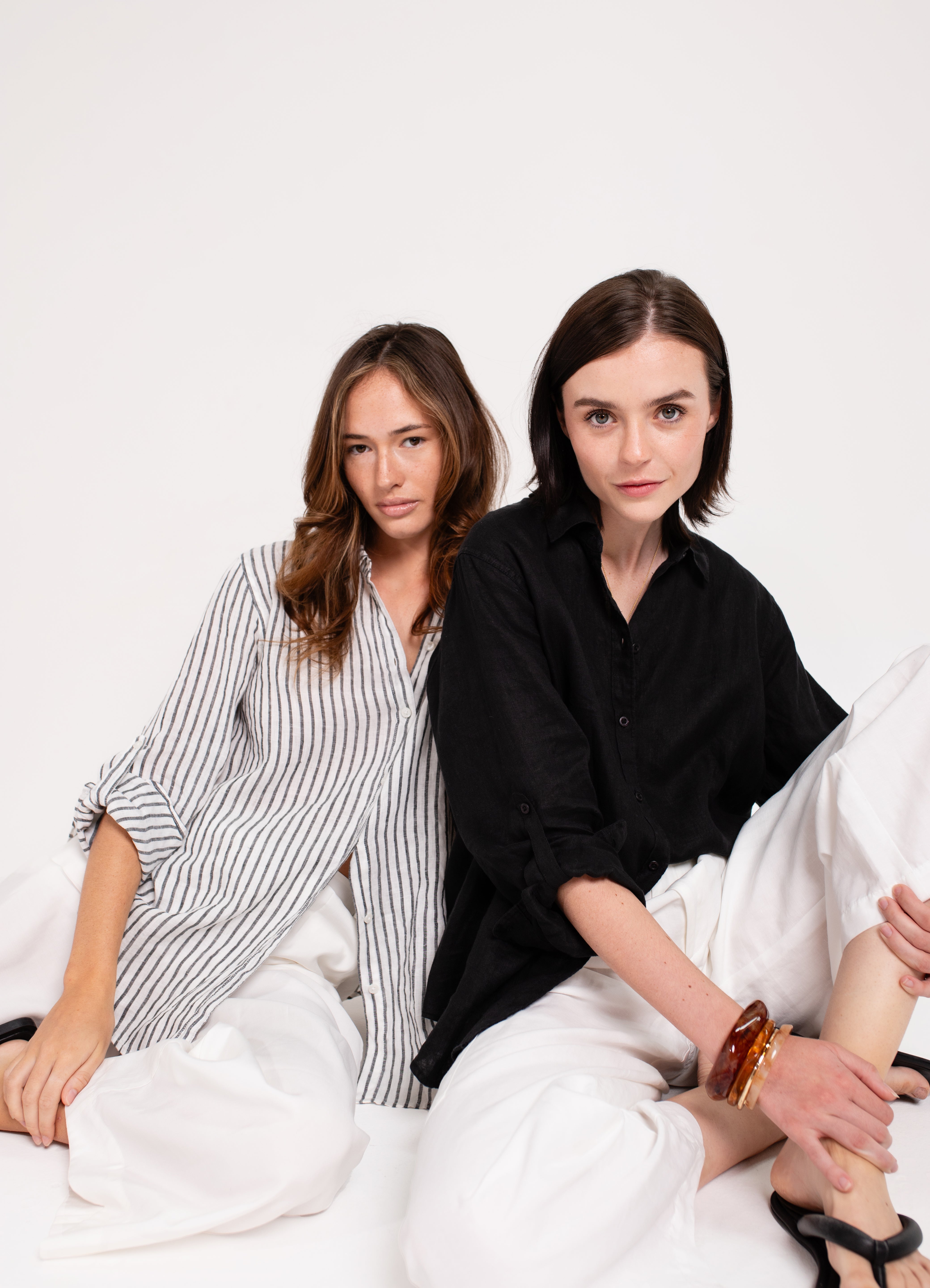 Two models wearing different outfits; one in a striped Hut boyfriend linen shirt and the other in a solid black Hut boyfriend shirt, against a white background.