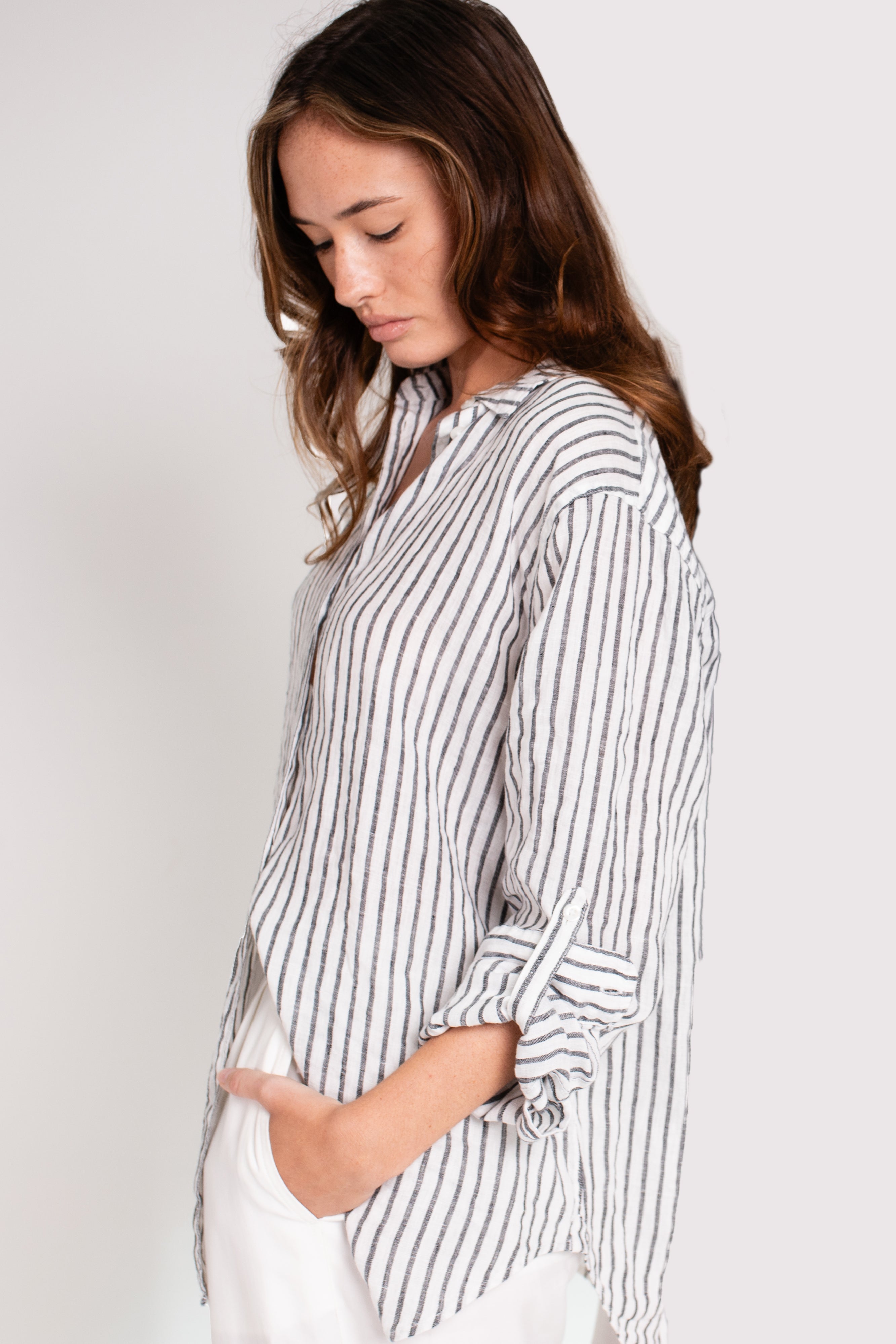 A woman wearing a Hut black and white striped boyfriend linen shirt with a scoop hem and tab sleeves.