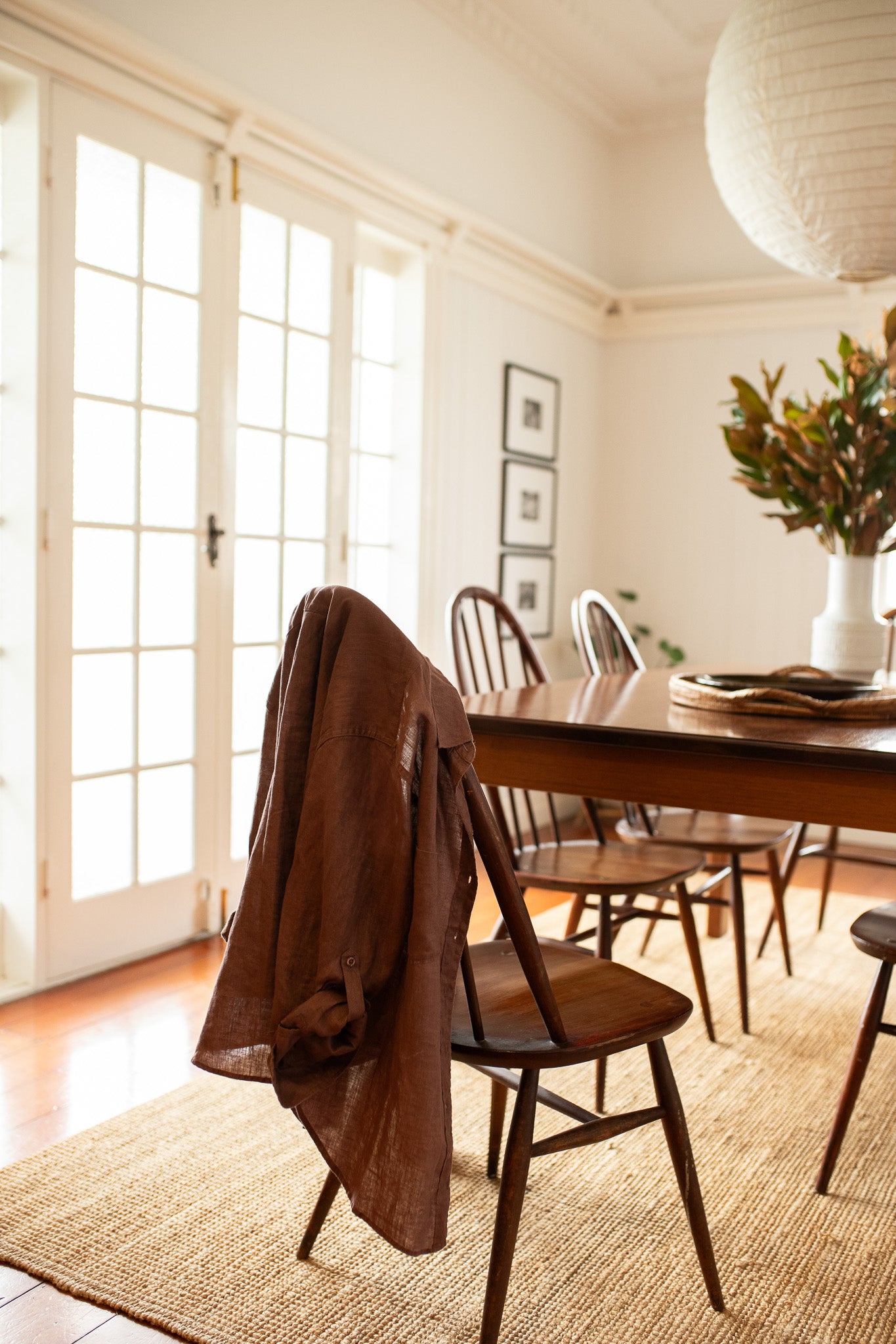 A brown Hut linen boyfriend shirt hanging on a chair in a room with a dining table and large windows.