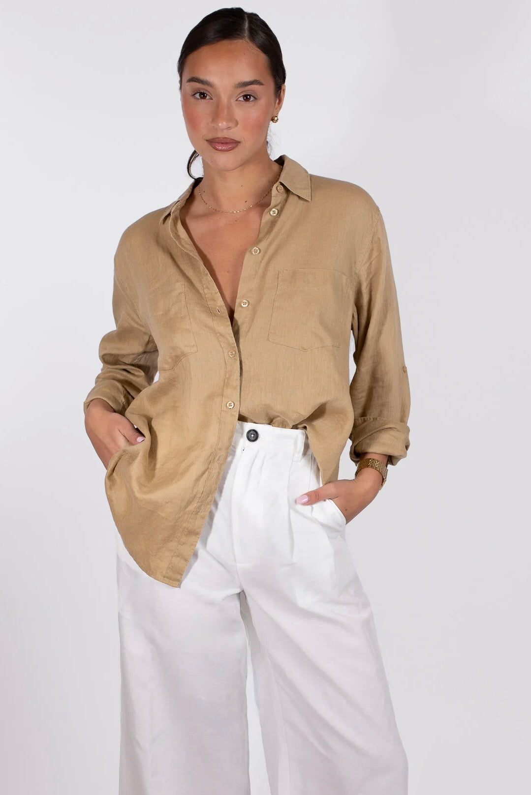 A woman wearing a Hut beige linen boyfriend shirt with a collar, button-up, two chest pockets and long sleeves, paired with white trousers.