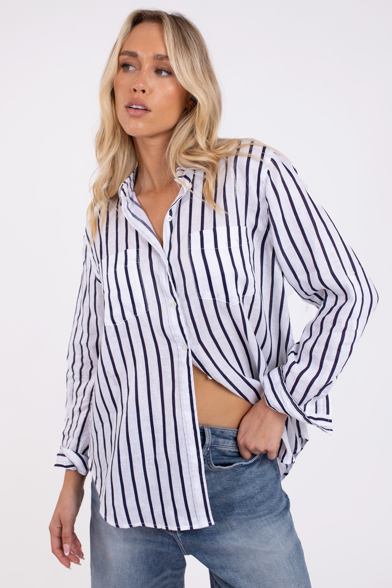 A woman wearing a navy and white striped linen shirt with a collar, button-up front, and long sleeves, paired with blue jeans.