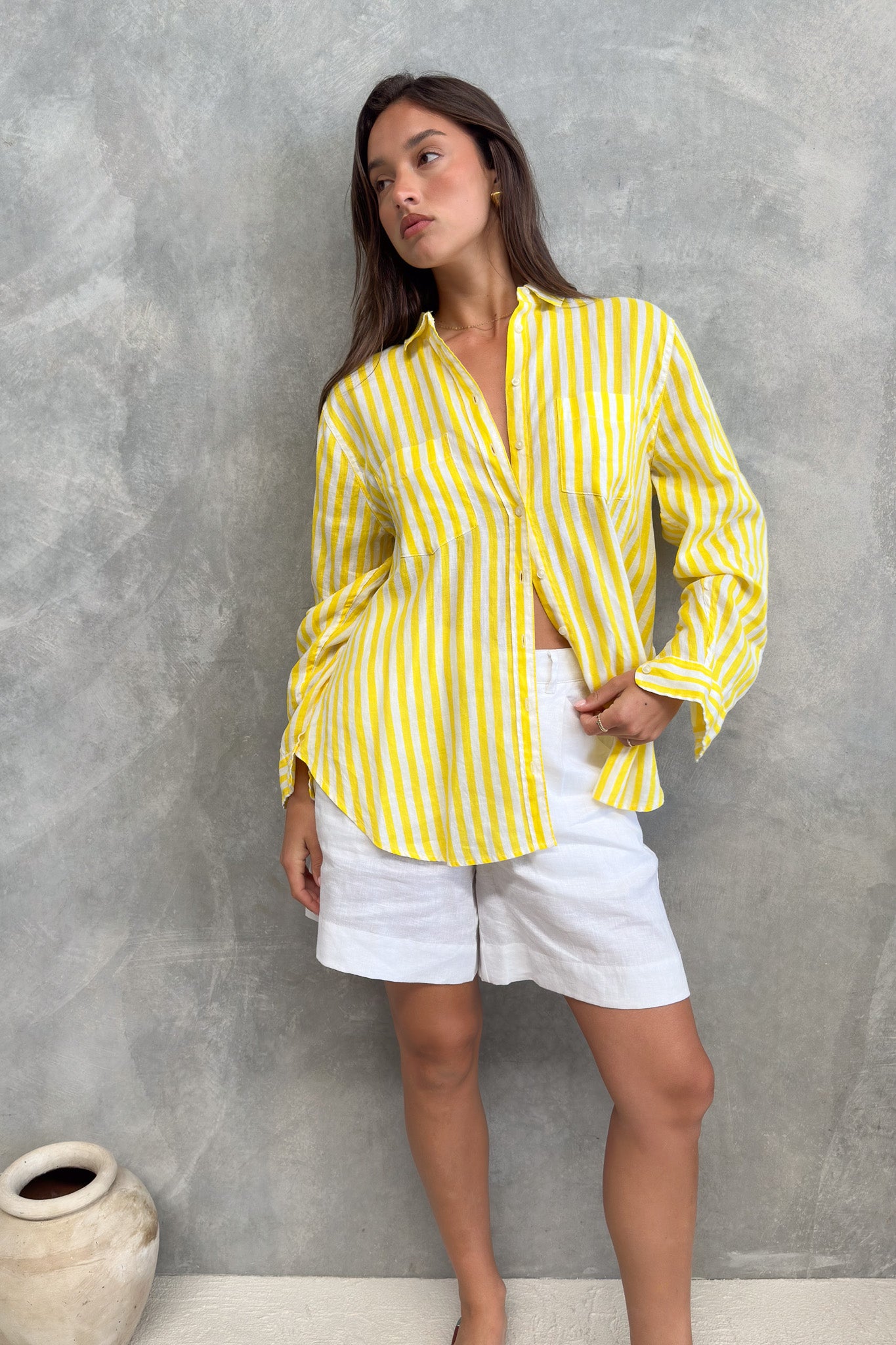 Model wearing a Hut clothing yellow and white stripe boyfriend linen shirt with white linen shorts and sleeves rolled down