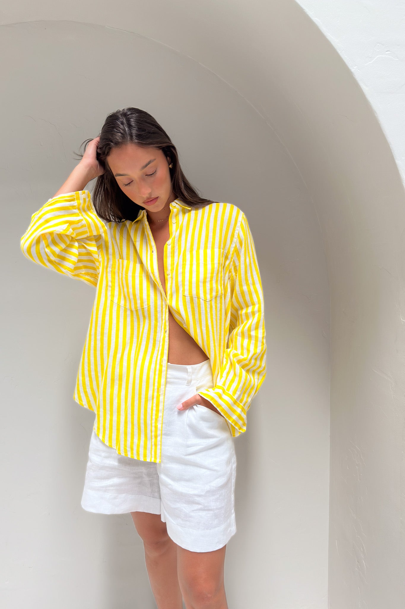Model wearing a yellow and white stripe linen boyfriend shirt with white linen shorts
