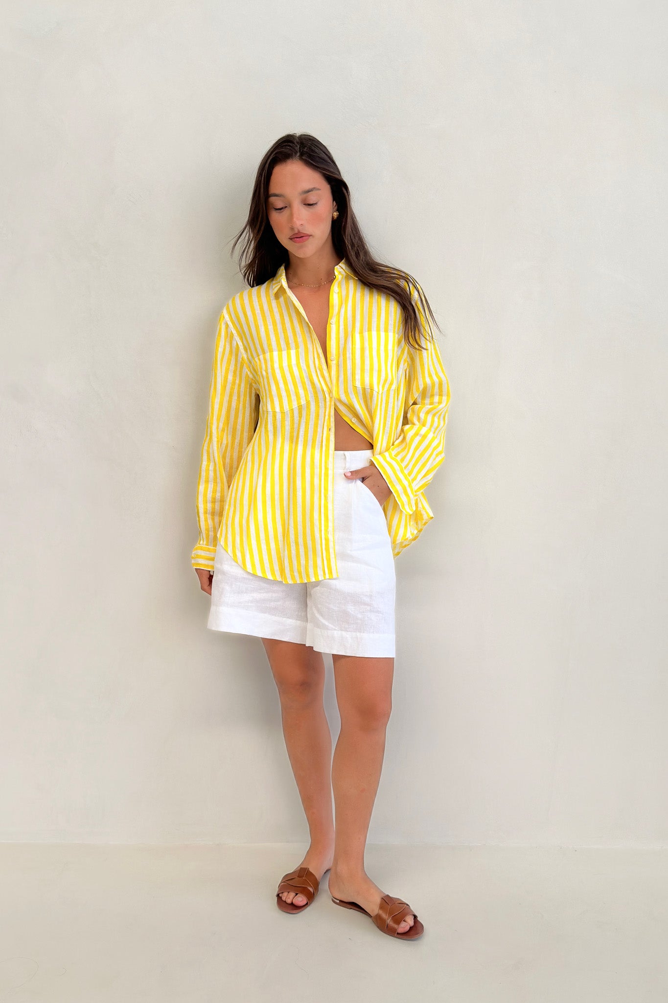 Model wearing yellow and white stripe linen boyfriend shirt with white linen shorts and sandals, sleeves rolled down