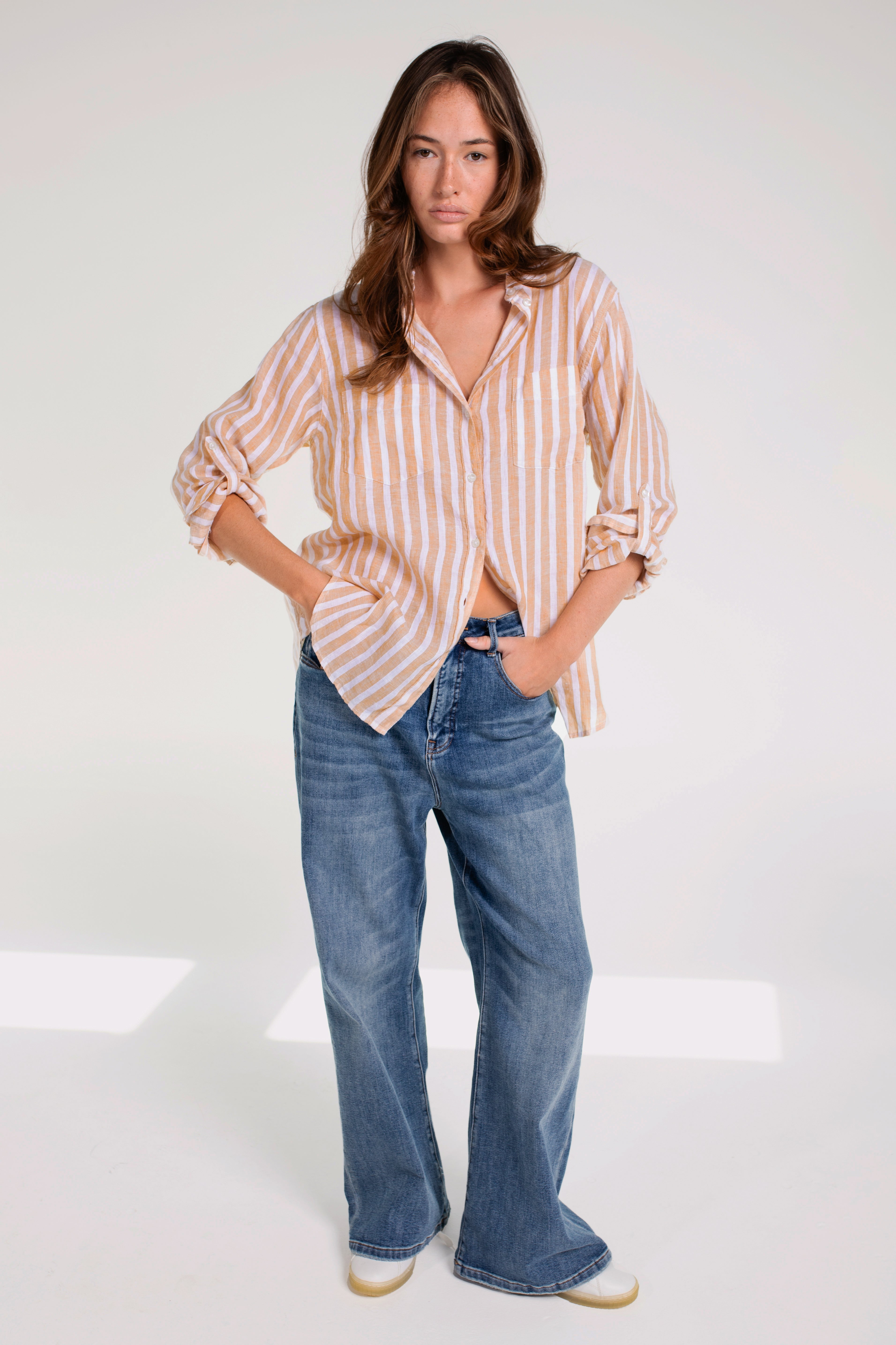 A woman wearing a striped hut boyfriend linen shirt with a collar, French seams, and a scoop hem, paired with blue jeans.