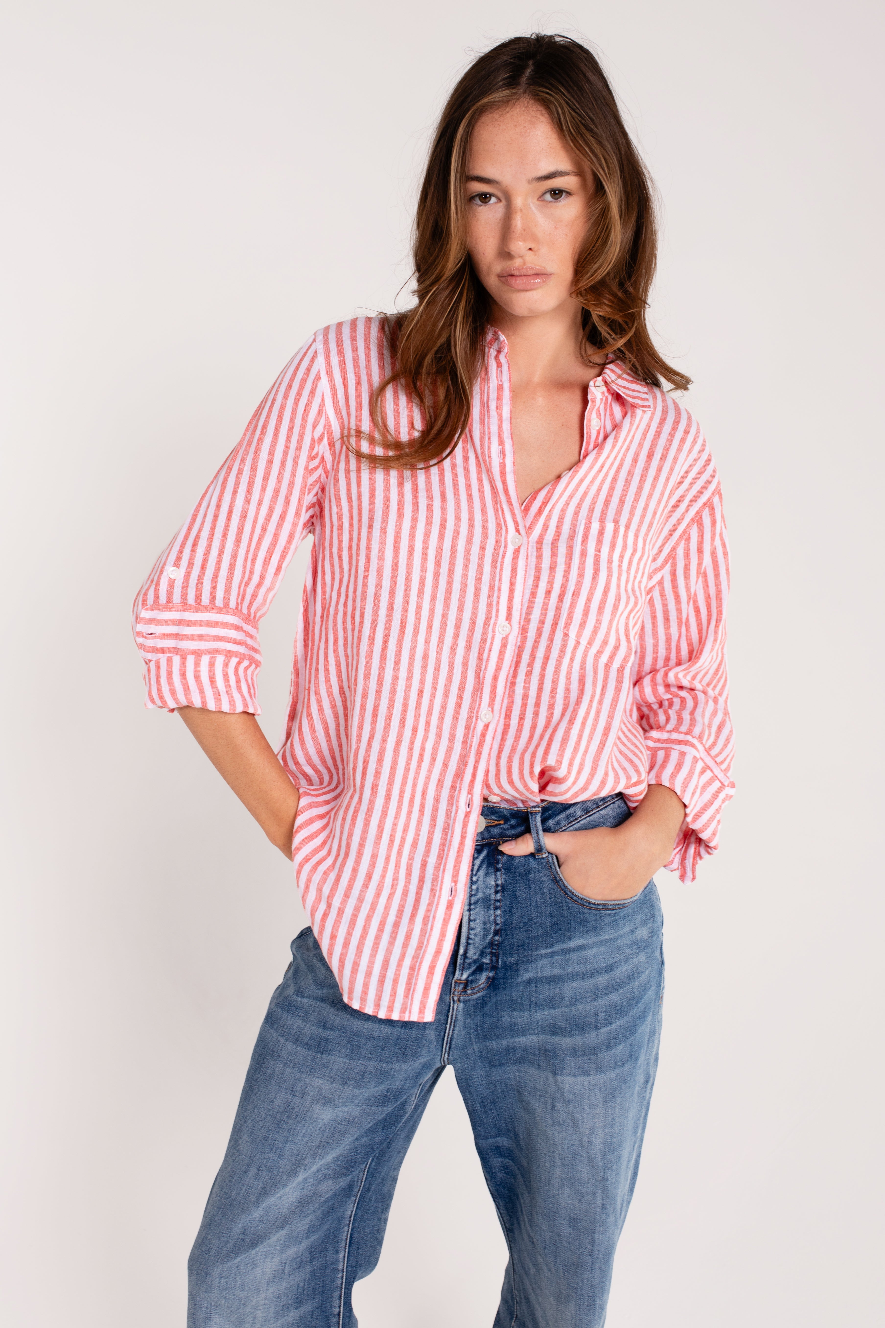 A woman wearing a Hut red and white striped boyfriend linen shirt with tab sleeves and a scoop hem, paired with blue jeans.