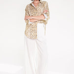 A woman wearing a Hut snake skin print boyfriend linen shirt in an oversized fit, paired with white trousers, standing against a white background.