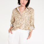 A woman wearing a snake skin print boyfriend linen shirt in an oversized fit with white trousers.