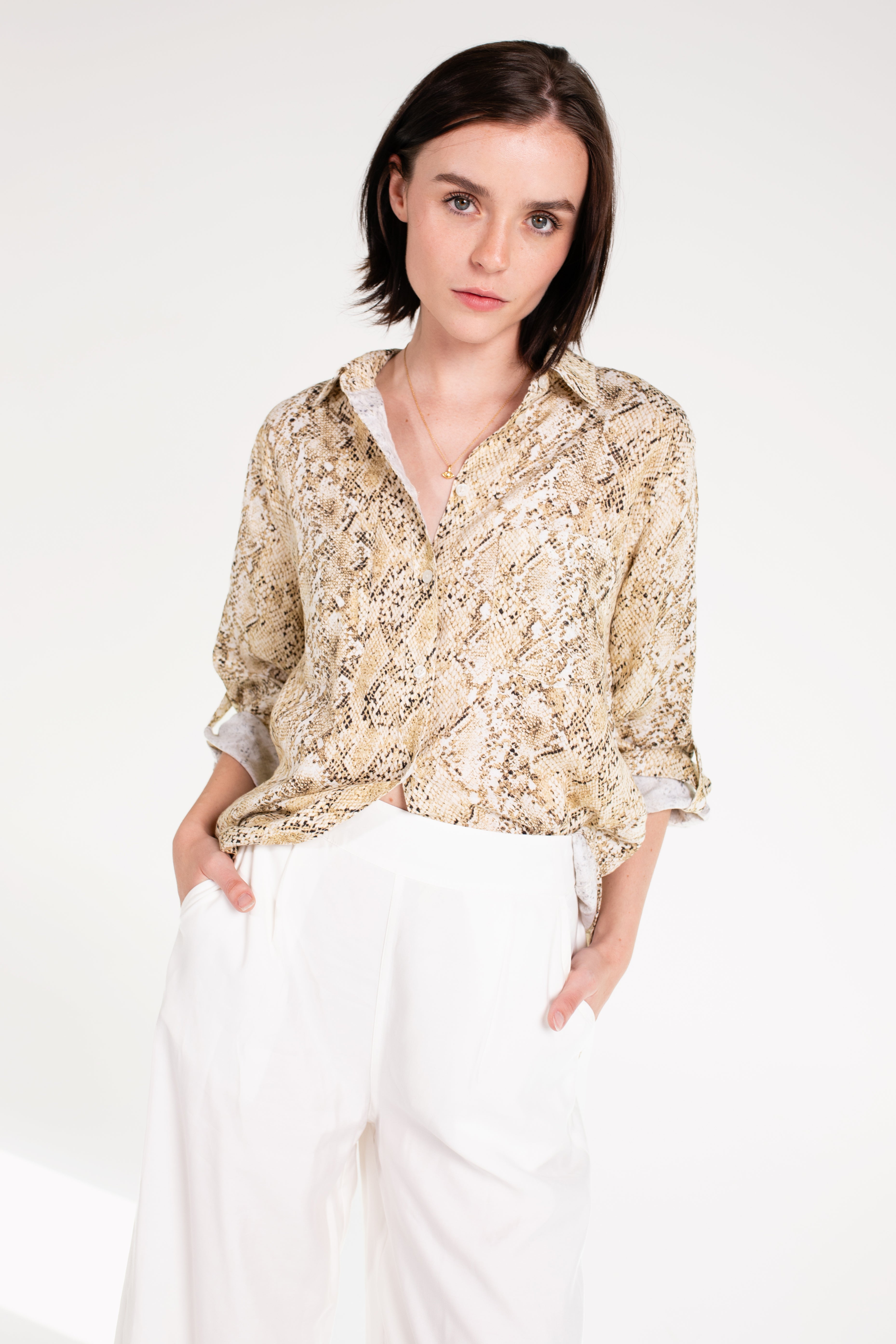 A woman wearing a snake skin print boyfriend linen shirt in an oversized fit with white trousers.
