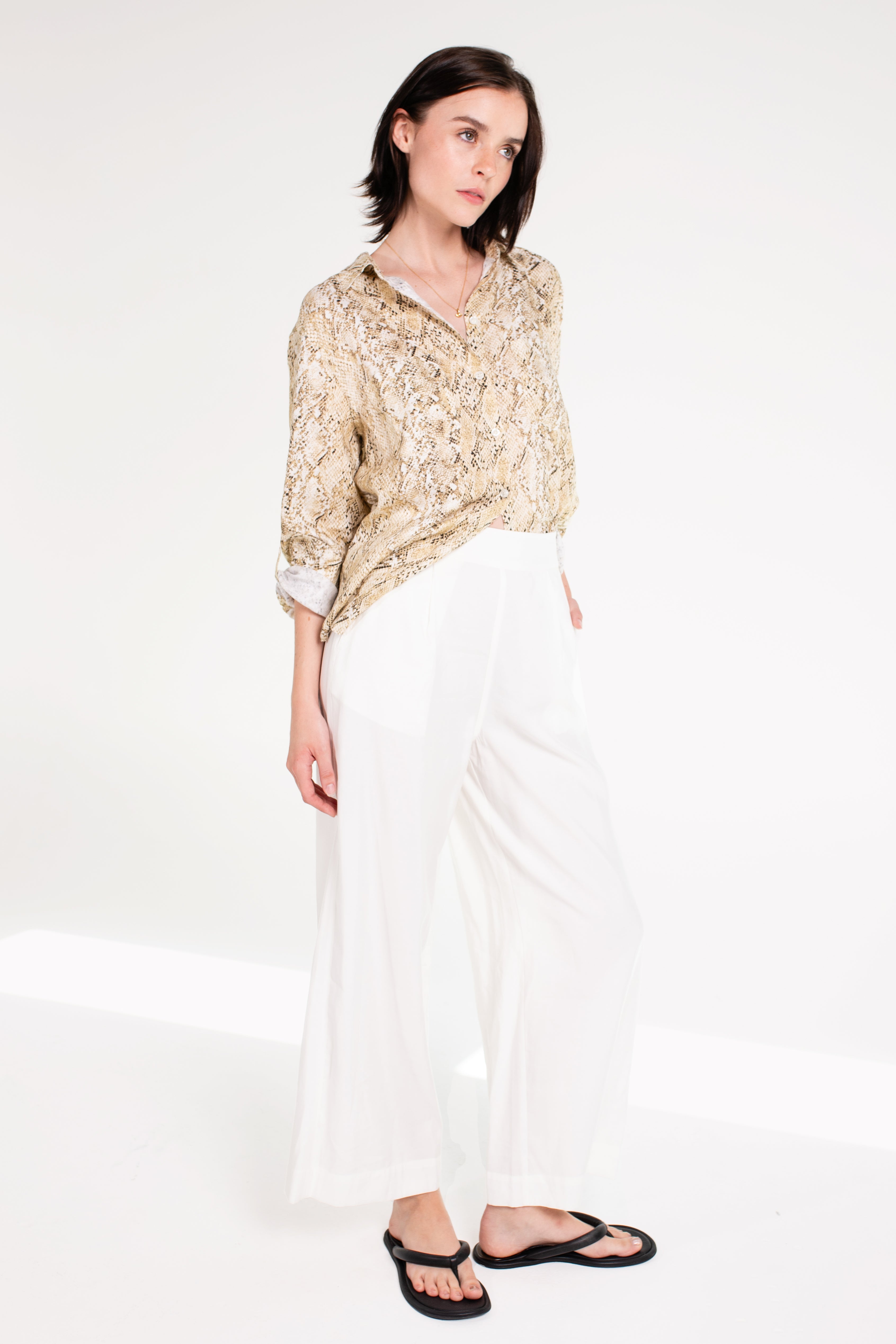 Woman wearing Hut Snake Skin Print Boyfriend Linen Shirt in an oversized fit and rolled sleeves with white trousers and black sandals