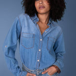 Woman wearing a blue Hut denim shirt and jeans against a plain background