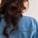 Close up of embroidery on a Hut blue denim oversized shirt with a neutral background