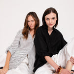 Two models wearing different outfits; one in a striped Hut boyfriend linen shirt and the other in a solid black Hut boyfriend shirt, against a white background.