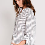 A woman wearing a Hut black and white striped boyfriend linen shirt with a scoop hem and tab sleeves.
