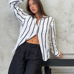 A woman wearing a black and white striped Hut boyfriend linen shirt with French seams and a scoop hem, paired with black shorts.
