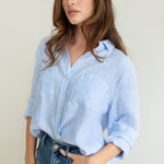 A woman wearing a baby blue striped linen boyfriend shirt with long sleeves and a scoop hem, paired with blue jeans.