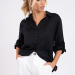 Model wearing Hut Clothing Black No Pocket Boyfriend Linen Shirt with tab sleeves rolled up and hands in pockets of white trousers 