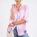 A woman wearing a Hut Clothing pink plaid boyfriend linen shirt oversized fit with collar, buttoned up, paired with blue jeans and a beige handbag.
