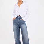 A woman wearing a white linen boyfriend shirt with a hidden placket, button-up front, and a classic collar, paired with blue wide-leg jeans.