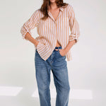 A woman wearing a striped hut boyfriend linen shirt with a collar, French seams, and a scoop hem, paired with blue jeans.