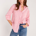 A woman wearing a Hut red and white striped boyfriend linen shirt with tab sleeves and a scoop hem, paired with blue jeans.